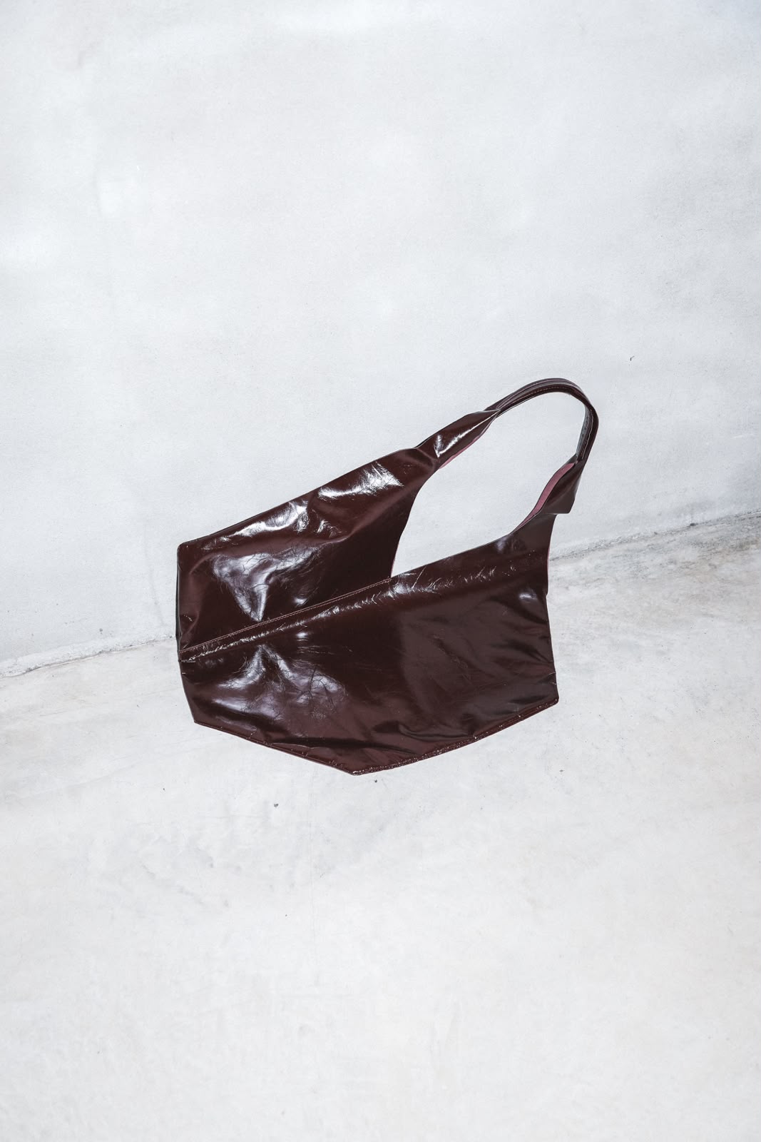 Burgundy patent leather shoulder bag against concrete