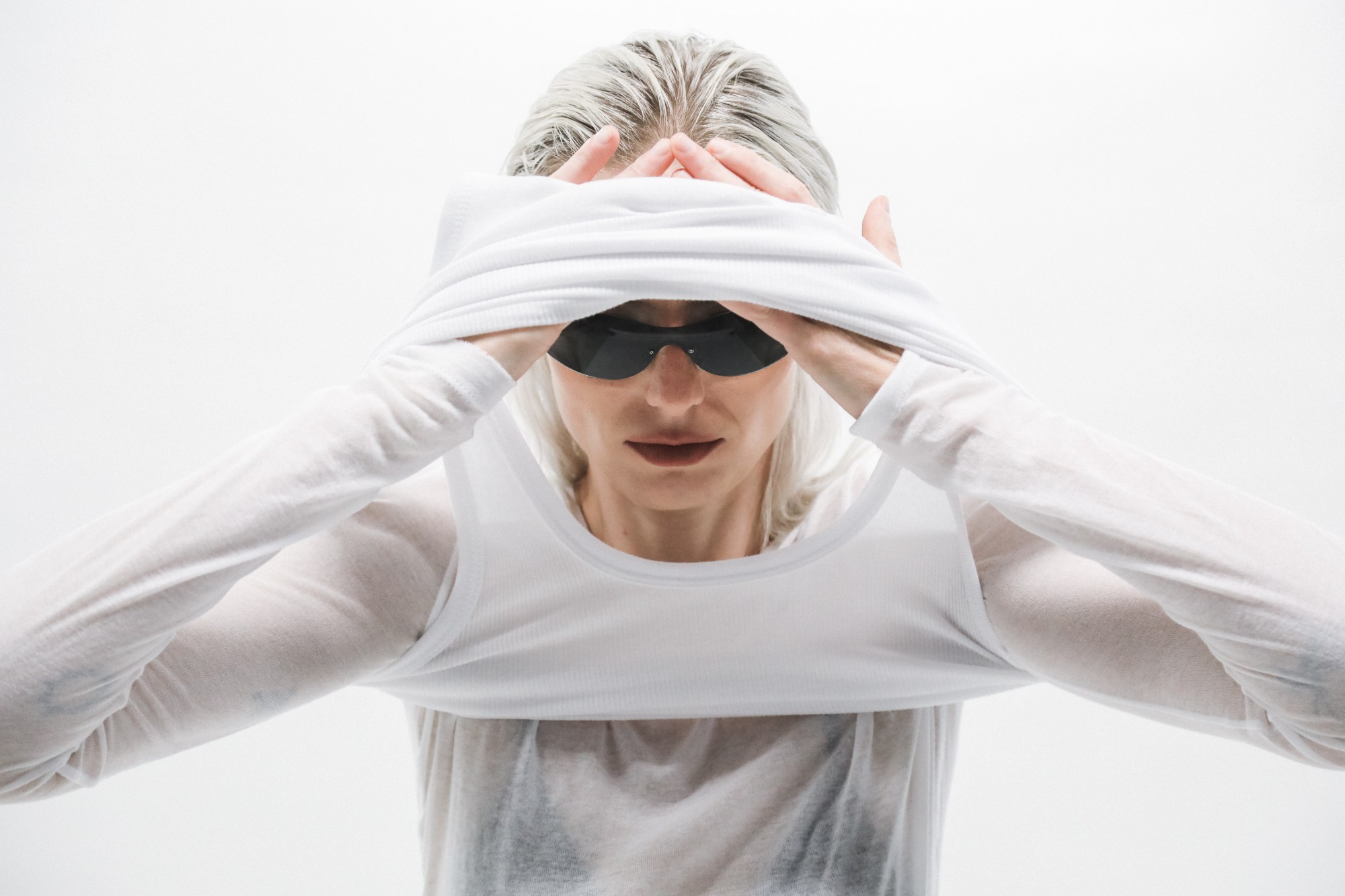 Model in white pulling a top over dark sunglasses