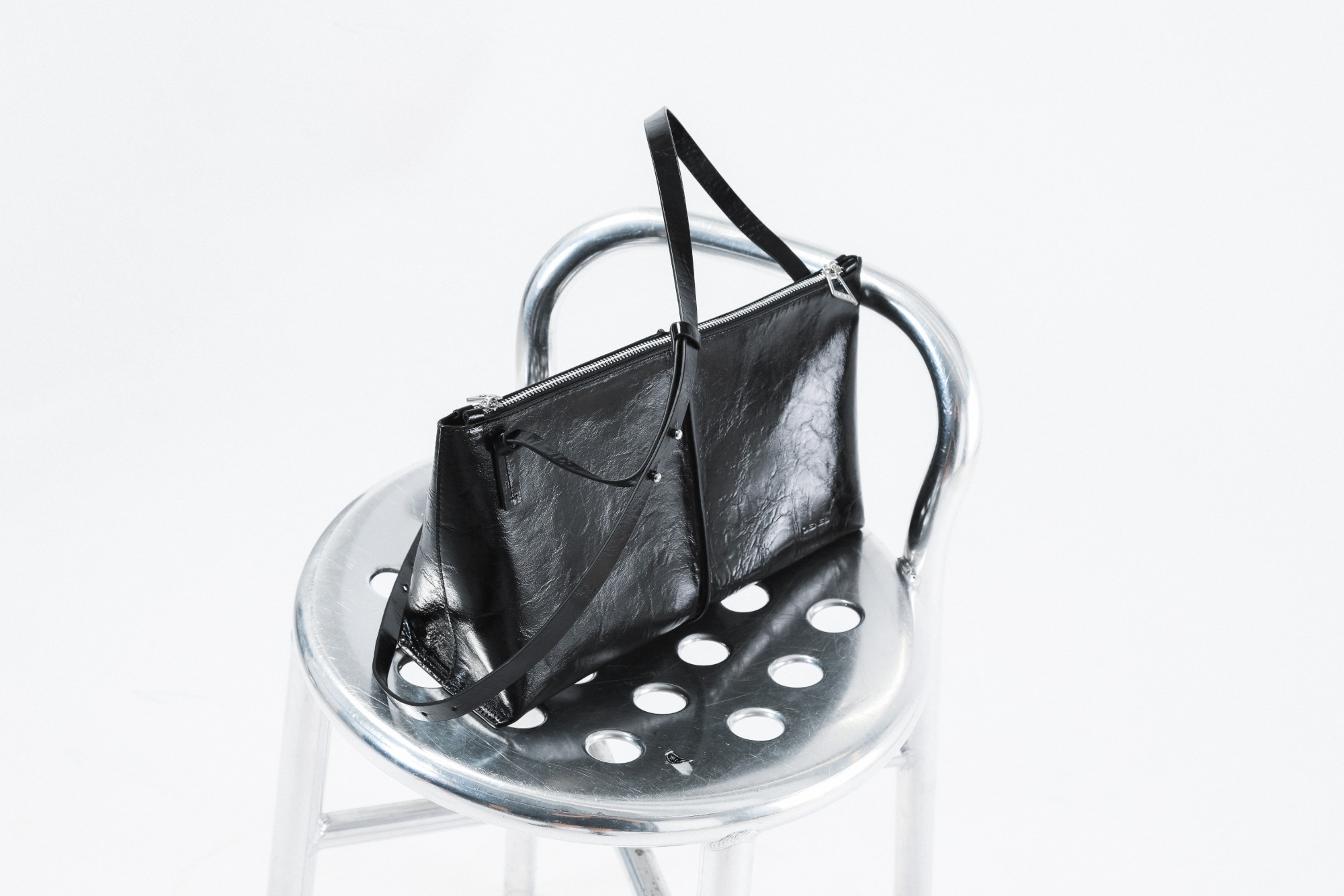 Black crinkled leather DIENÈE shoulder bag resting on a metal chair